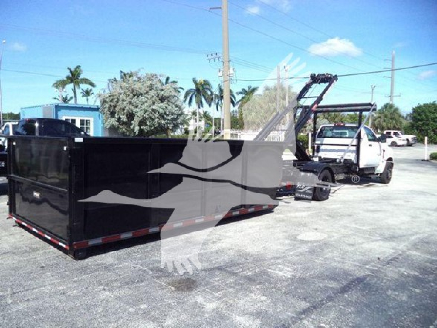 Truck in a lot with a large black dump bed trailer attached to a tow rig. Side view shows a Chevrolet Silverado 6500HD or similar with a gooseneck? There are no legible labels visible due to watermark across image.