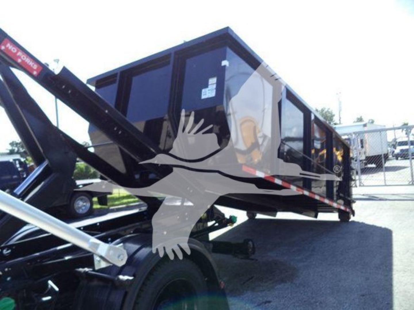 Truck trailer dump bed in a yard showing a black dump body with hydraulic arm and side panels. Text visible: none legible.