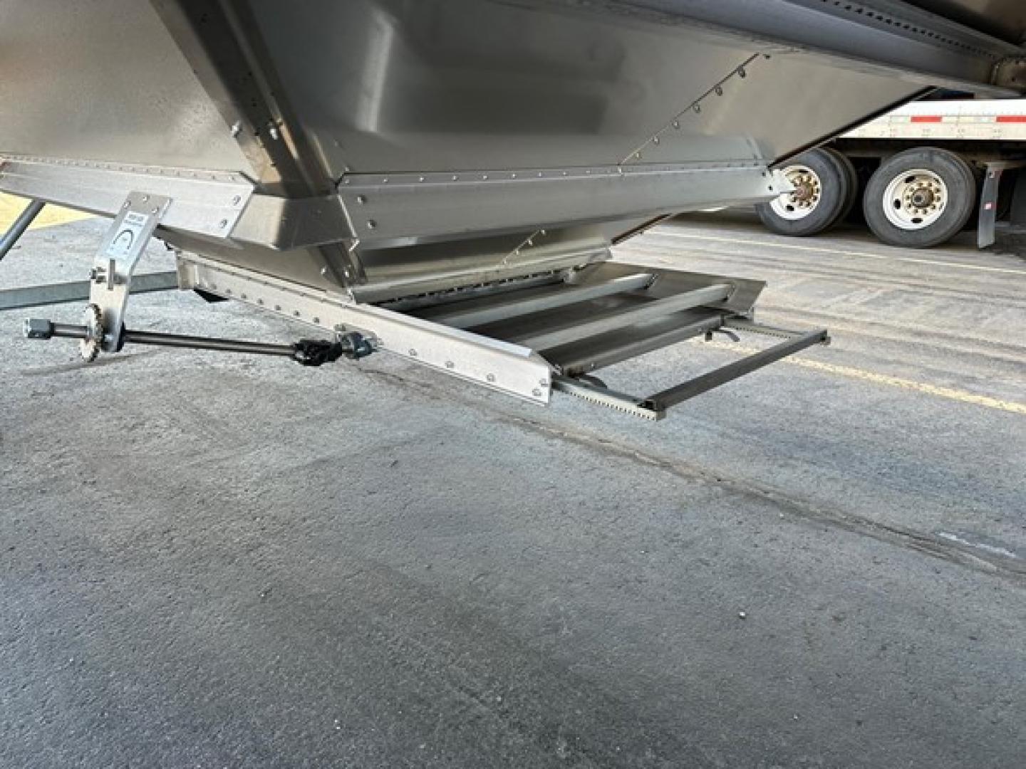 Hopper-type trailer unloading chute and underside showing a fold-out access ladder and hitch area on a 2025 Stoughton grain trailer.