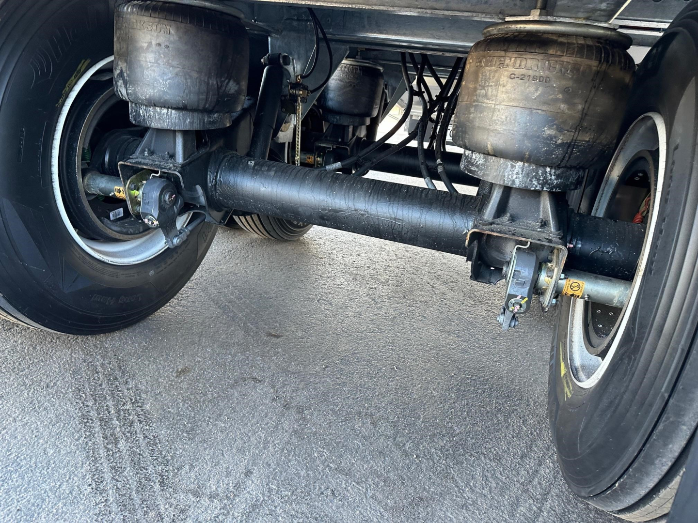 Trailer rear underside showing solid axle, air ride suspension parts, two large cylindrical air tanks, leaf springs, and differential housing; visible wheels and tires.