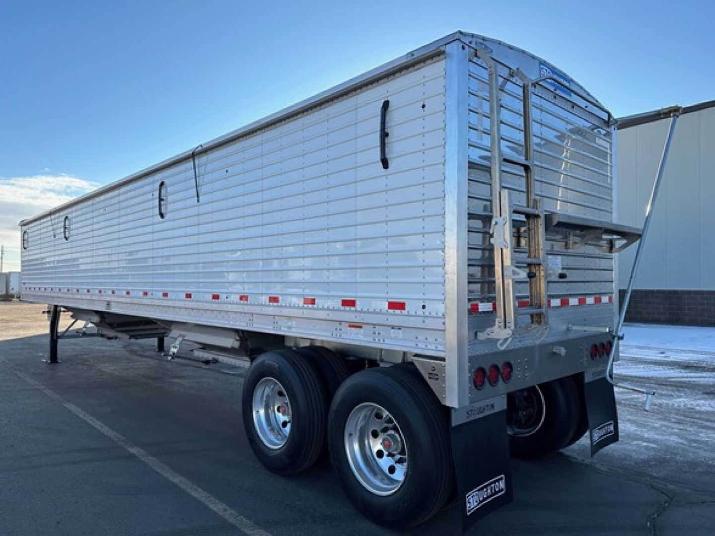 Stoughton grain trailer in service showing aluminum side panels, dual rear axles, and rear loading chute with ladders.