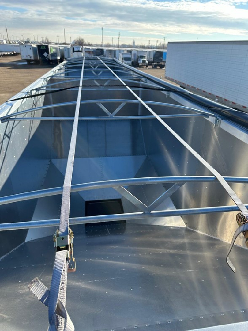 Stoughton grain trailer underside midsection showing galvanized steel hopper with crisscross bracing and tie-down straps along the length.
