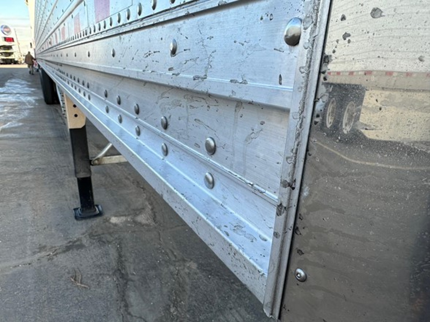 Trailer side panel of a Stoughton grain trailer showing riveted aluminum panels with bolts and support legs.
