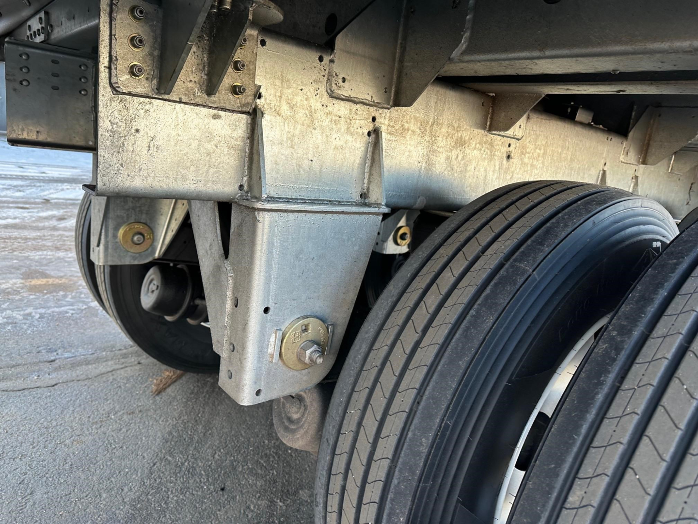 Trailer undercarriage showing suspension hanger and air ride components with dual wheels and steel frame.