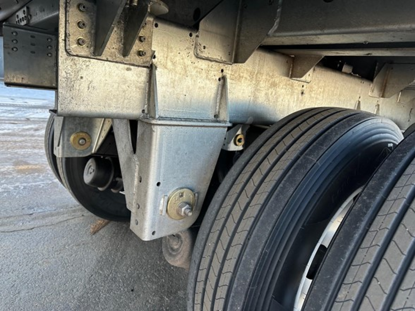 Trailer undercarriage showing suspension bracket and dual tires of a Stoughton grain trailer, metallic components and bolts visible.