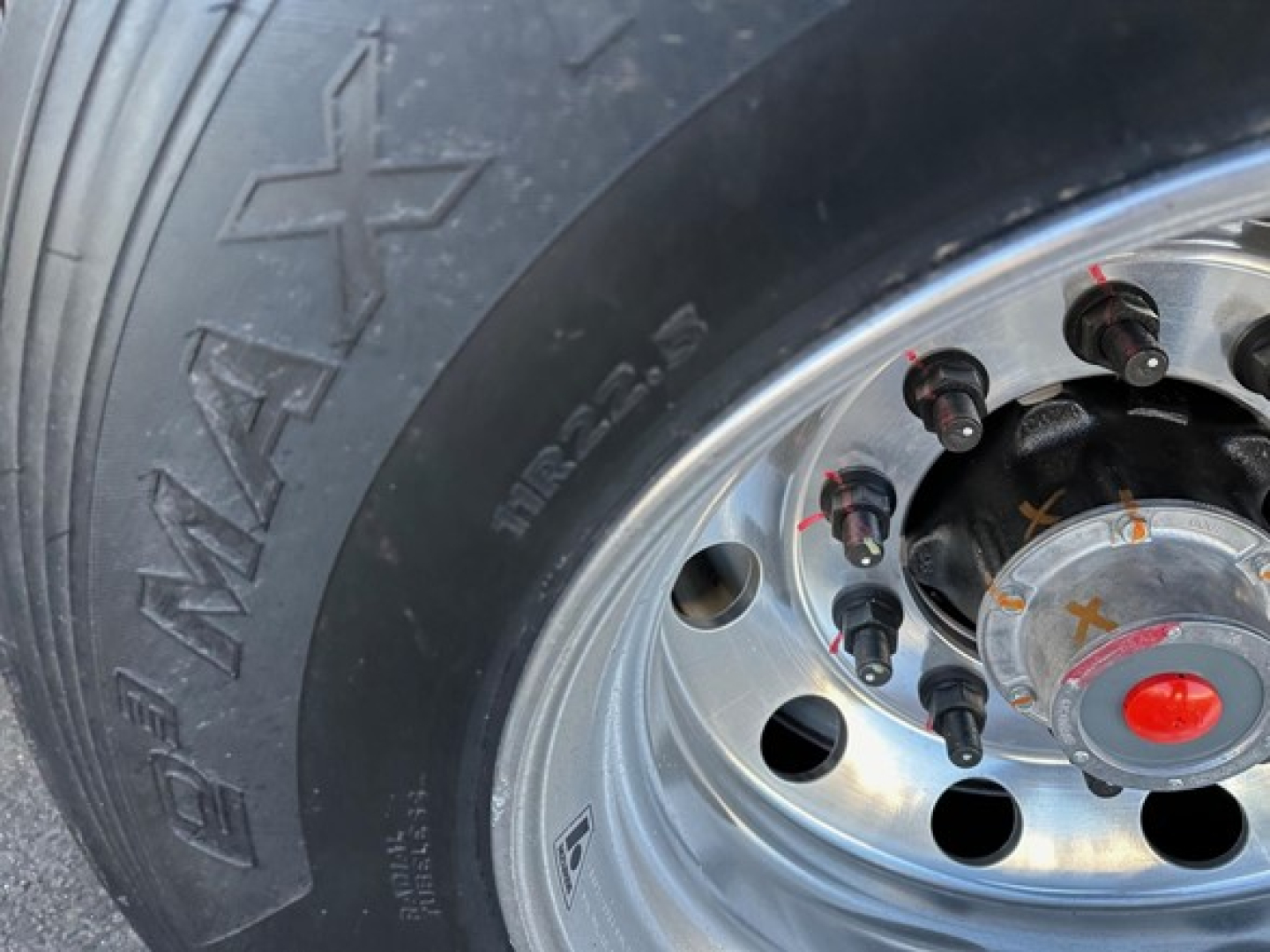 Wheel of a Stoughton grain trailer with chrome hub and lug nuts visible; tire sidewall shows 'XR' branding and wheel has multiple circular holes.
