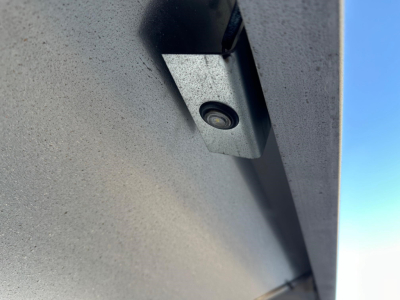 Trailer component showing a small, round fastener embedded in a metal surface, with a textured gray paint and a blue sky in the background.