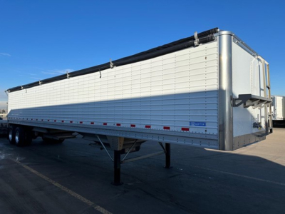 Stoughton grain trailer (hopper) side view showing aluminum body, black tarp, dual rear ramps, landing gear, and wheel axles.