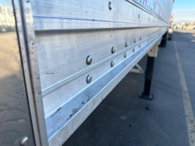 Stoughton grain trailer side panel showing riveted aluminum construction with bolts and support legs in view.