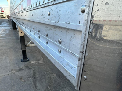 Trailer side panel of a Stoughton grain trailer showing riveted aluminum panels with bolts and support legs.