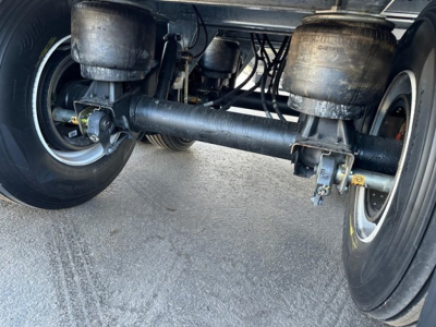 Hopper trailer undercarriage showing suspension beam and wheel axles with dual tanks and hoses visible.