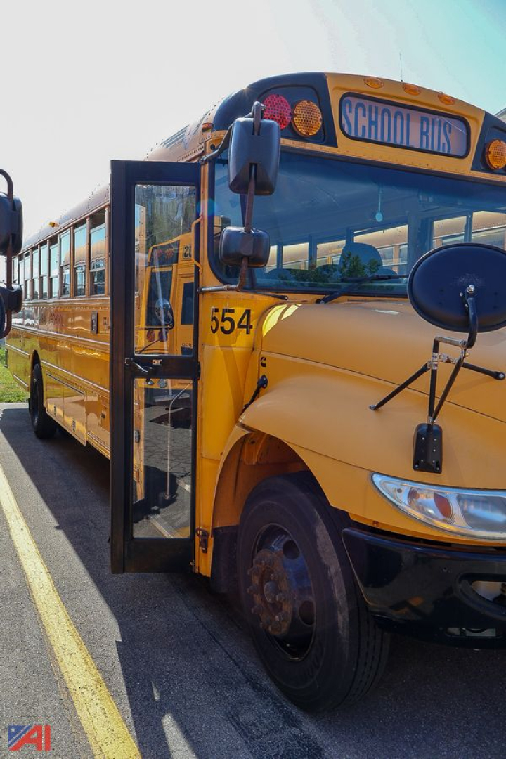School bus front corner with open door, yellow CE-series bus, number 554 visible on bumper, School Bus sign on top, blue accents.