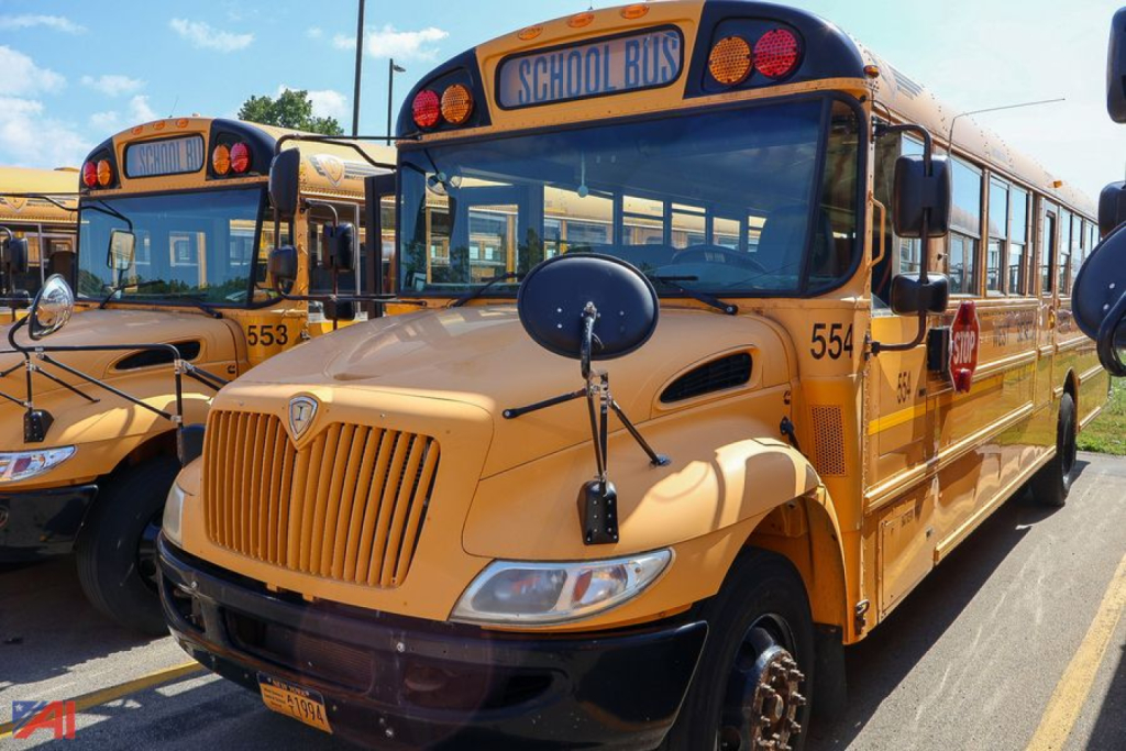 Yellow IC Corporation CE Series school bus with front view and 'SCHOOL BUS' sign on top, multiple buses in background.