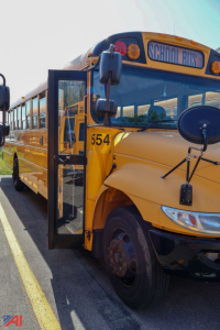 School bus front corner with open door, yellow CE-series bus, number 554 visible on bumper, School Bus sign on top, blue accents.
