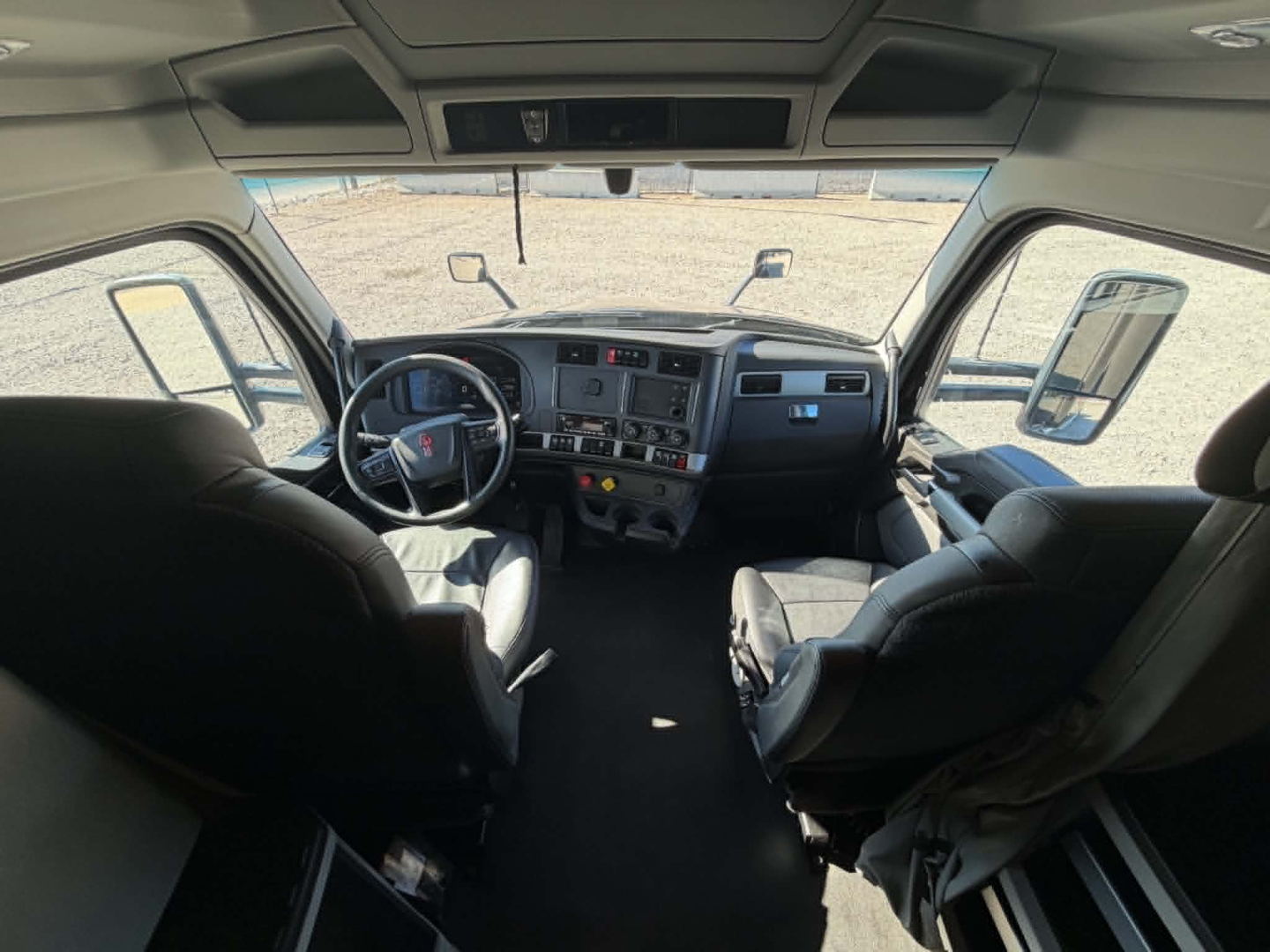 Kenworth T680 cabin interior, front windshield view showing steering wheel, dashboard, driver and passenger seats, side mirrors, and overhead storage.