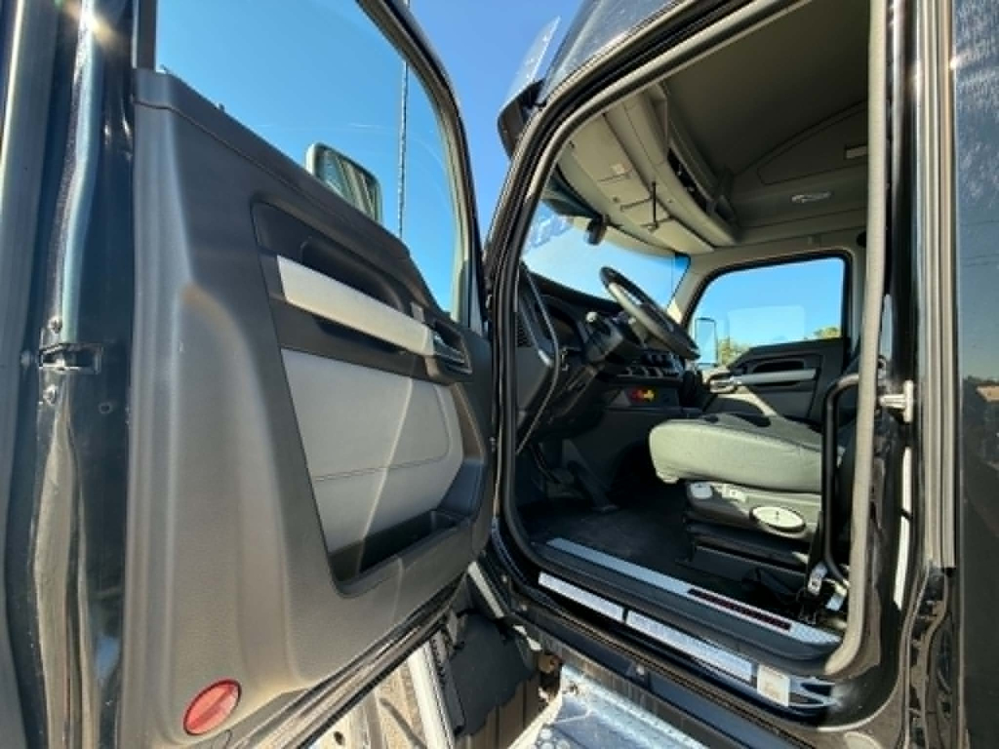 Cab interior of a 2023 Kenworth T680 Conventional Sleeper from driver side door open showing steering wheel dash and seat.