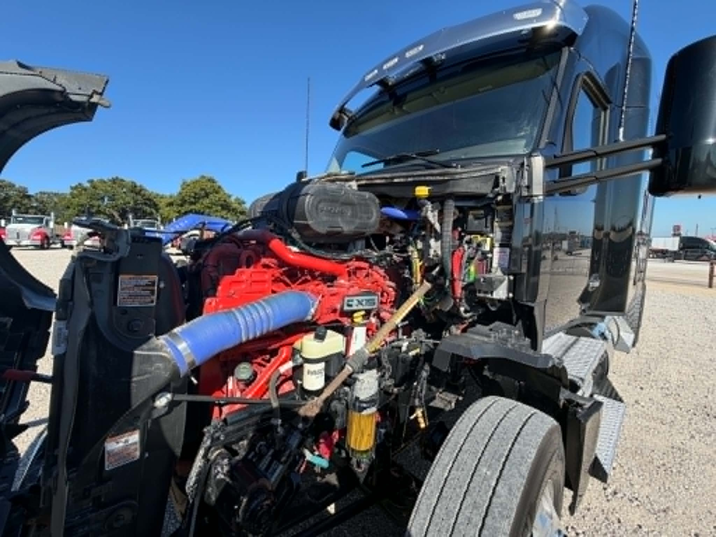 Kenworth T680 engine bay with exposed red engine and blue hoses, cab all-black, front grill visible
