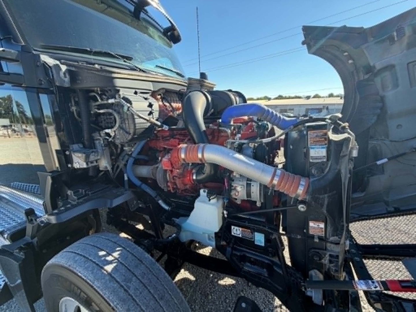 Kenworth T680 engine bay showing red engine, blue and gray hoses, radiator, coolant reservoir, and intake tubing.