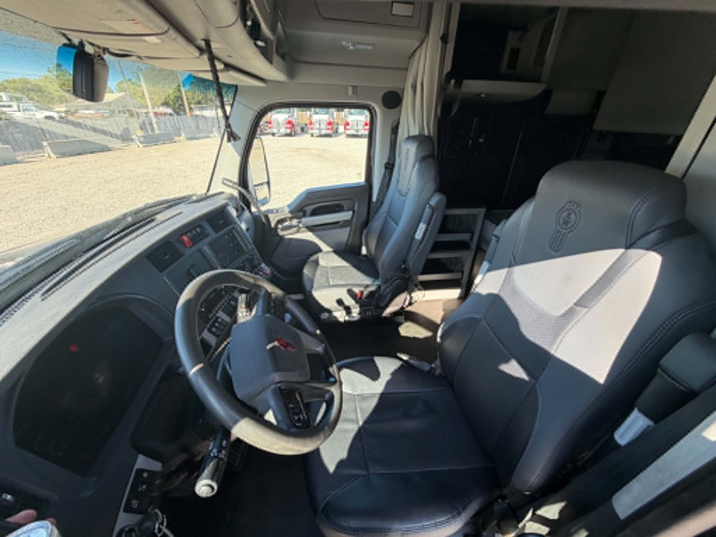 Kenworth T680 interior driver seat and dashboard view showing steering wheel, driver and passenger seats, and cabin area, with overhead storage and dashboard controls visible.