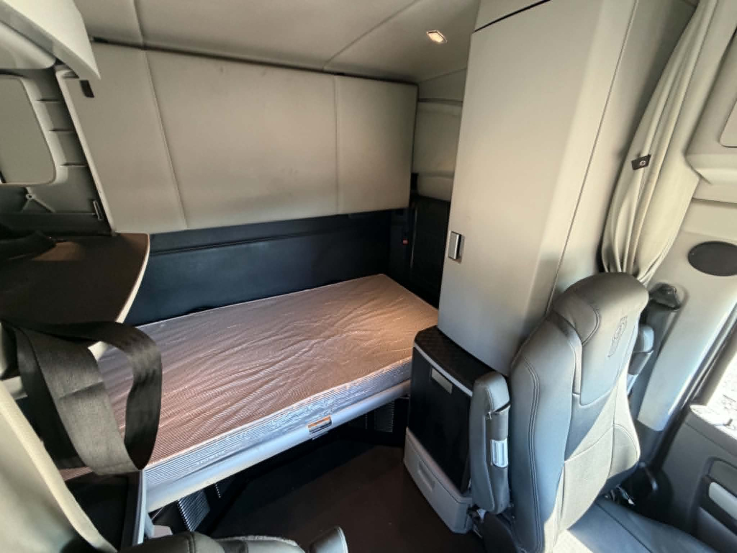 Kenworth T680 sleeper cab interior showing bunk bed area with mattress, side cabinet, and gray upholstery.