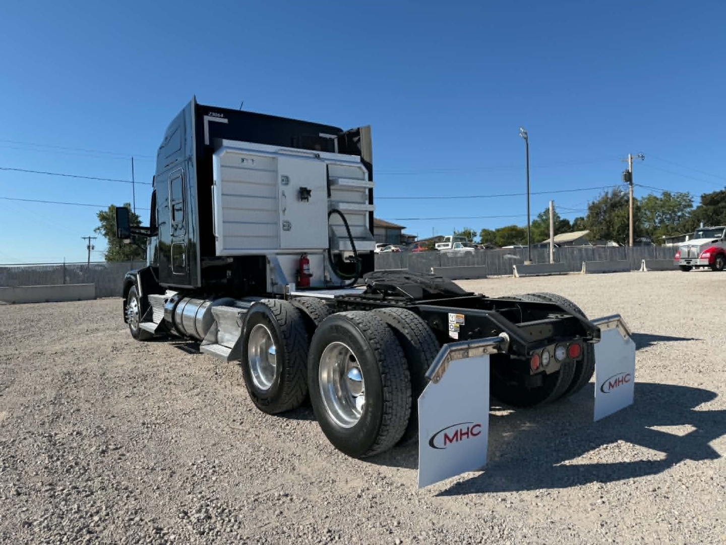 Kenworth T680 tractor rear view showing dual rear axles and mud flaps with MHC logo, sleeper cab, exhaust stack, and fifth wheel area.