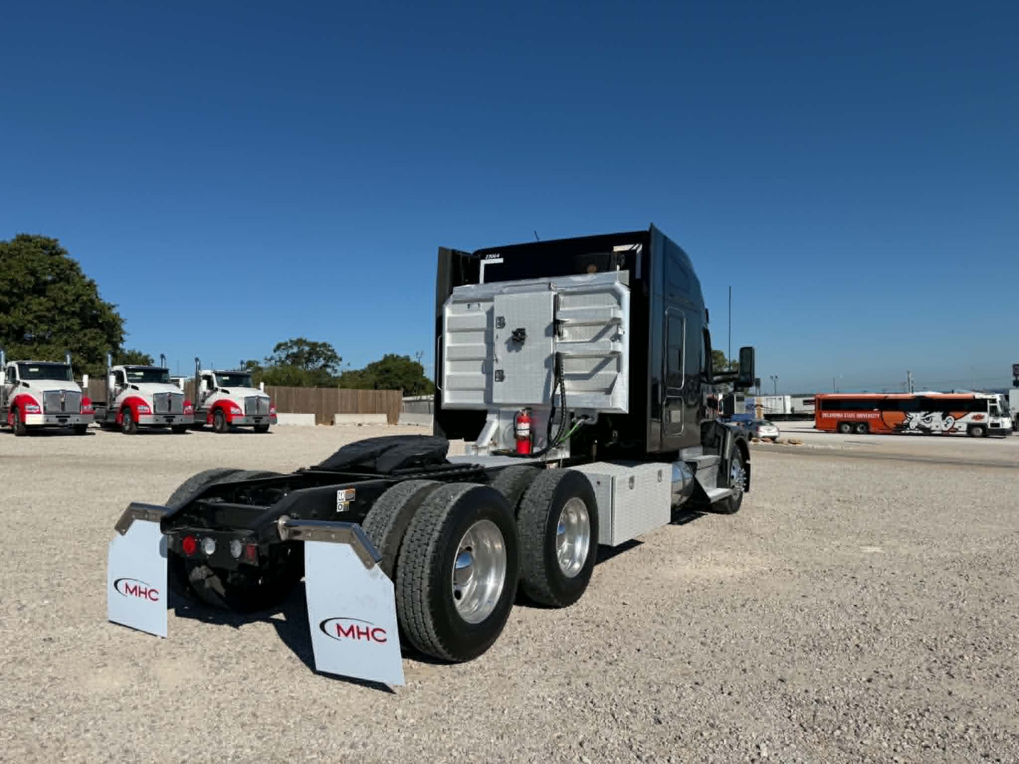 Kenworth T680 truck chassis rear view showing fifth wheel and dual rear axles, gas tank, and mud flaps with MHC branding.