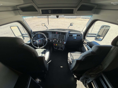 Kenworth T680 cabin interior, front windshield view showing steering wheel, dashboard, driver and passenger seats, side mirrors, and overhead storage.