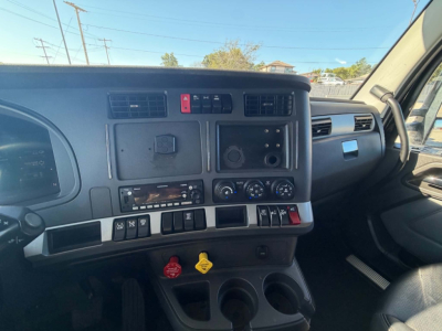 Kenworth T680 dash area showing central console with switches, knobs, and vents; steering wheel on left, cup holders and dashboard storage visible.