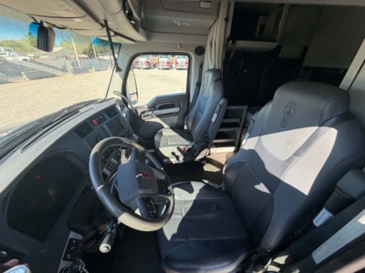 Kenworth T680 interior driver seat and dashboard view showing steering wheel, driver and passenger seats, and cabin area, with overhead storage and dashboard controls visible.