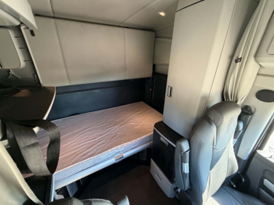 Kenworth T680 sleeper cab interior showing bunk bed area with mattress, side cabinet, and gray upholstery.