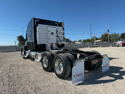 Kenworth T680 tractor rear view showing dual rear axles and mud flaps with MHC logo, sleeper cab, exhaust stack, and fifth wheel area.