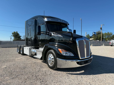 Kenworth T680 semi-truck in a gravel lot, front-left view. Visible text includes Kenworth emblem on grill, headlights, chrome bumper, side mirrors, and fuel tanks.