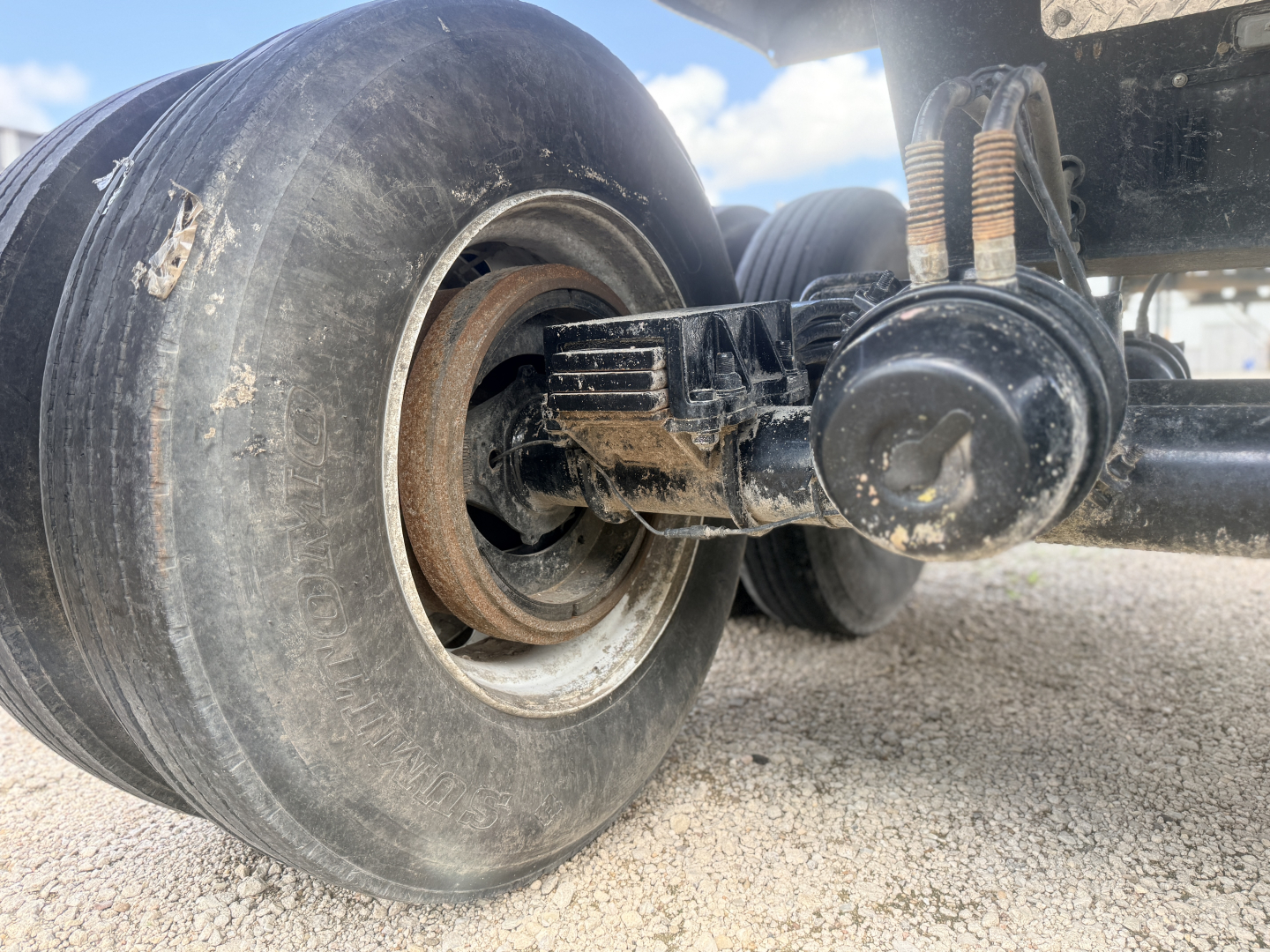 Rear dual-axle trailer suspension with air bag and leaf spring, large rubber tire, drum hub and mounting components visible.