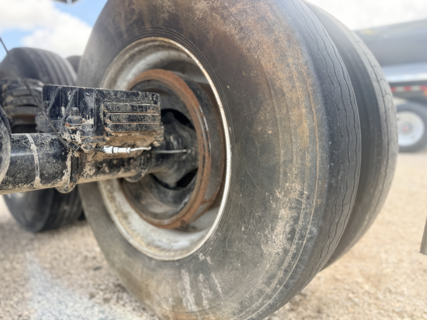 Trailer wheel hub showing a metal rim with rust and a black axle component; tire treads worn; dirt and mud on wheel area.