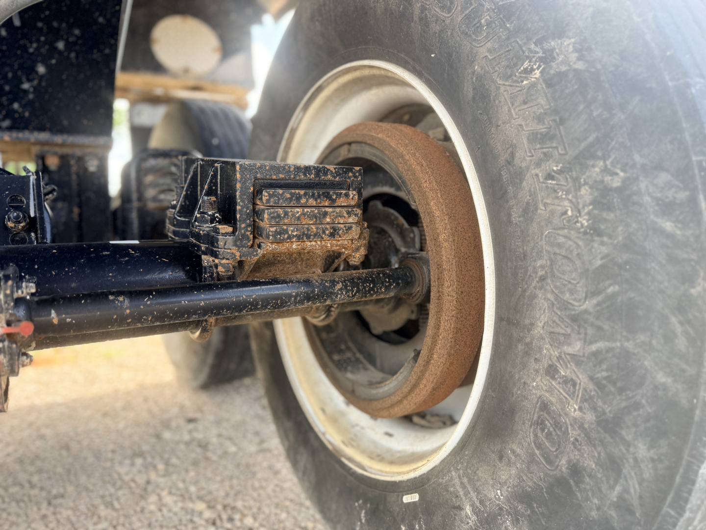 Trailer undercarriage with wheel, tire, and rust-colored brake drum visible; leaf spring and mounting hardware in view.