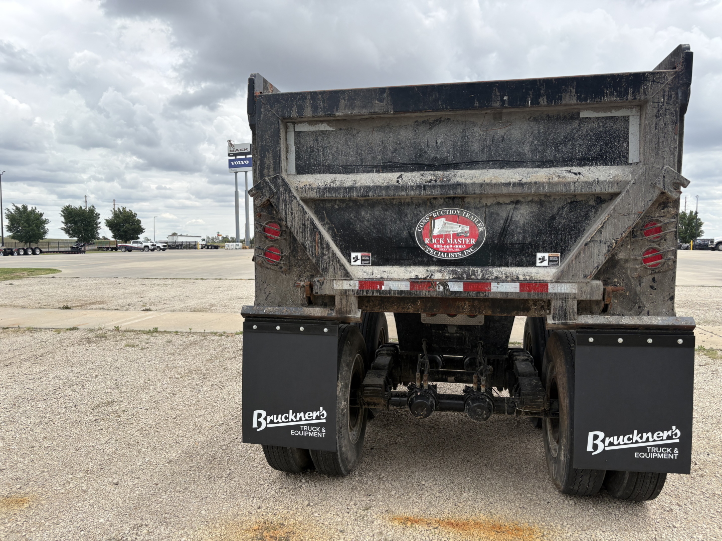 Dump trailer rear view showing mud and dirt, with Bruckner's mud flaps and rear lights; hydraulic hitch and dual axles visible.