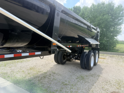Dump trailer with tandem axles showing wheels and black dump bed; side view of hitch and suspension visible.