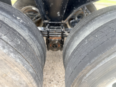 Trailer axle close-up showing dual tires and suspension components in view under a dump trailer.