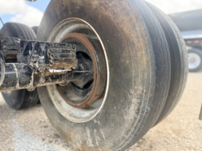 Trailer wheel hub showing a metal rim with rust and a black axle component; tire treads worn; dirt and mud on wheel area.