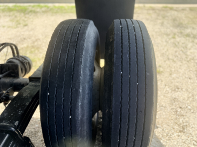 Trailer wheel pair in view showing two black tires with tread grooves, part of a dump trailer undercarriage.