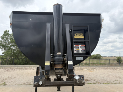 Dump trailer front view showing hitch assembly and vertical chute with warning labels.