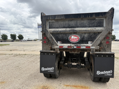 Dump trailer rear view showing mud and dirt, with Bruckner's mud flaps and rear lights; hydraulic hitch and dual axles visible.