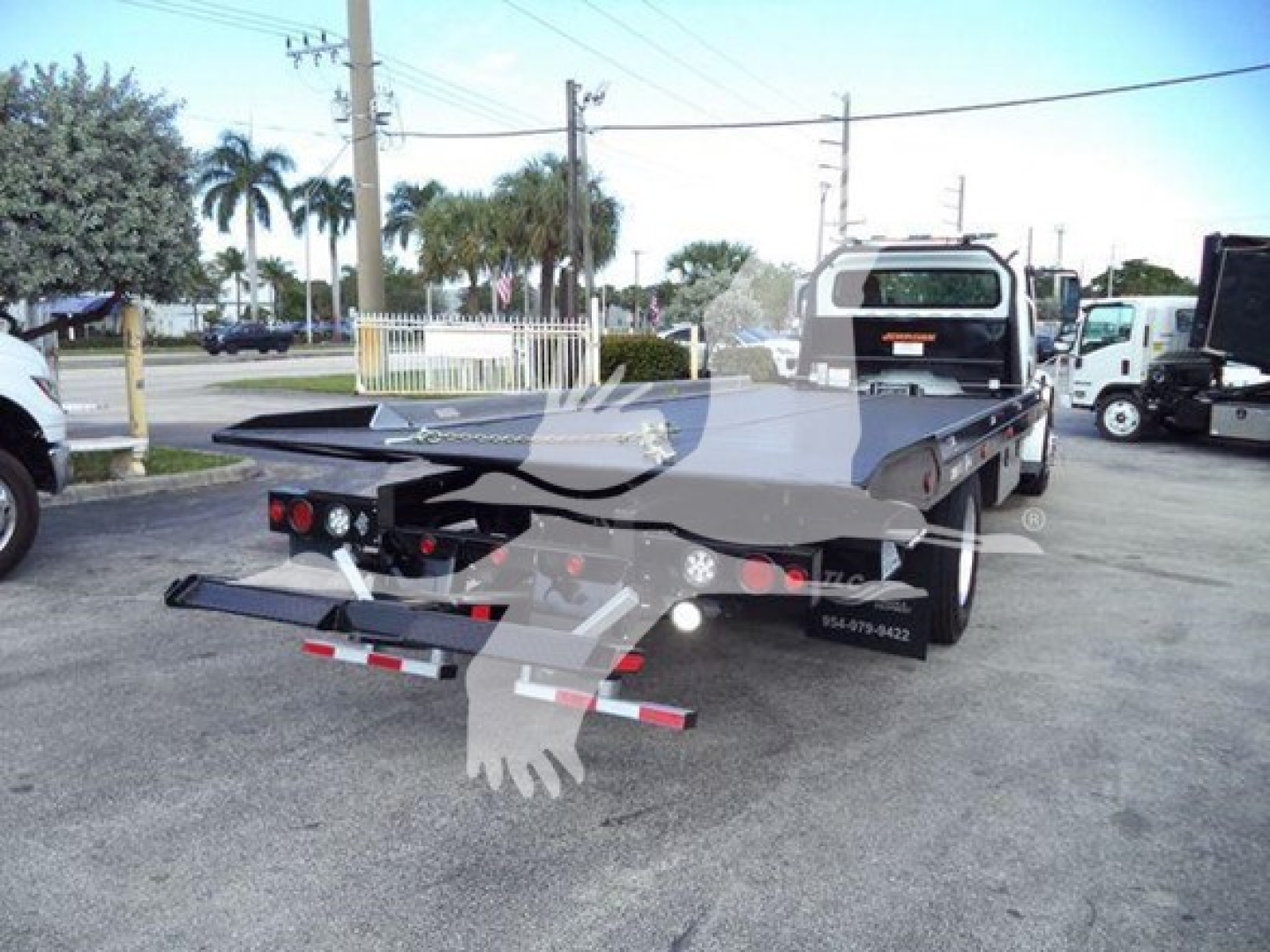 Flatbed tow truck rear view showing bumper lights and gooseneck hitch, Freightliner roll-back tow bed in parking lot.