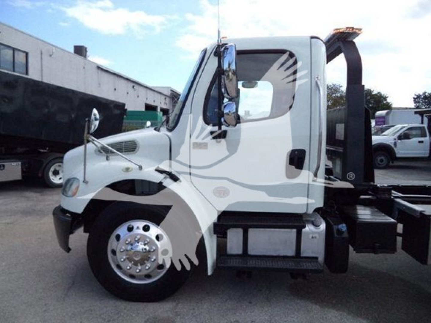 Truck cab side view of a 2019 Freightliner Business Class M2 106 rollback chassis showing cab door, mirrors, front fender, wheel, and hydraulic rollback boom mounting.