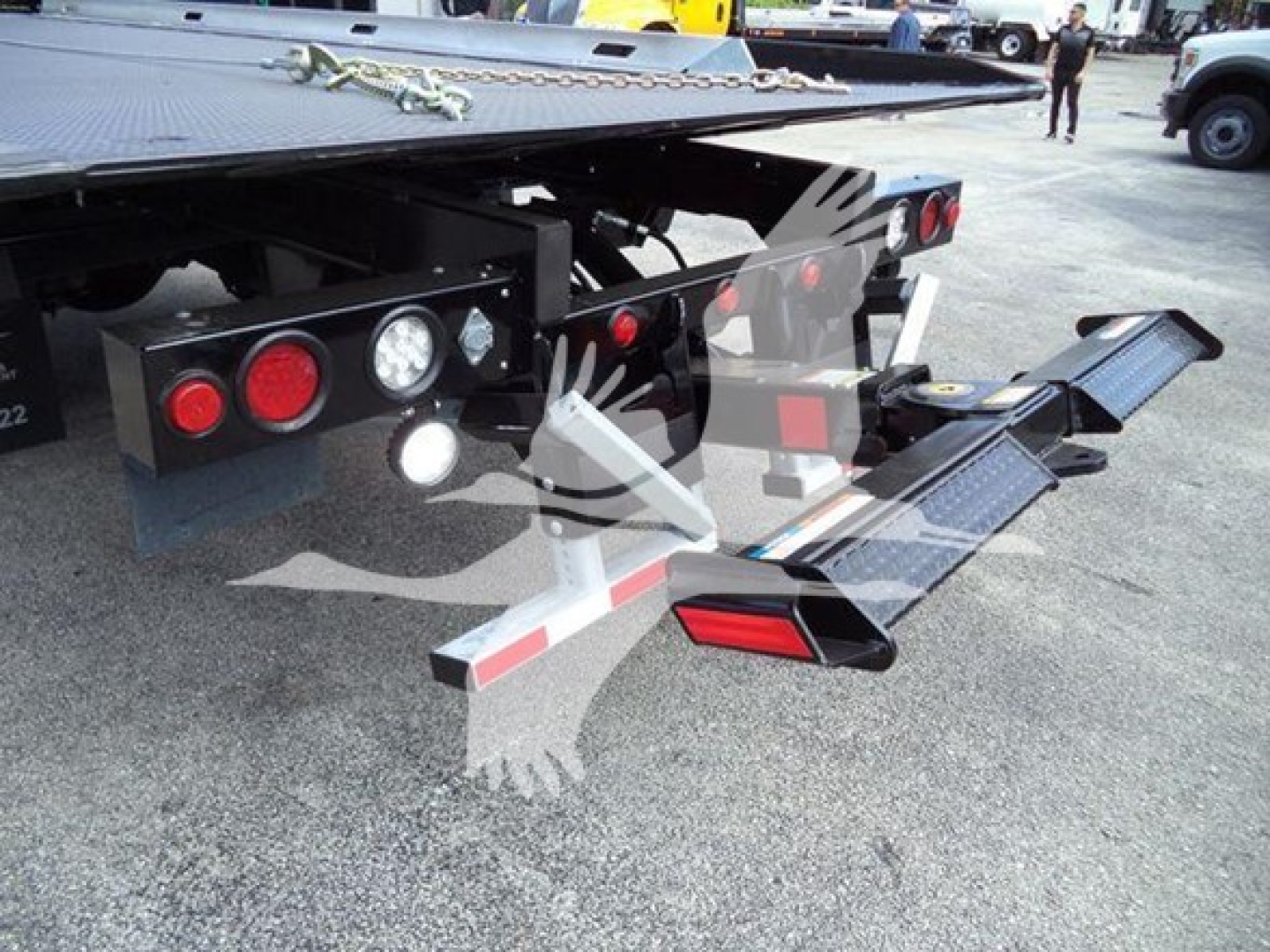 Freightliner Business Class M2 106 rollback truck rear showing hydraulic lines, taillights, and fold-out ramp in the concrete yard.