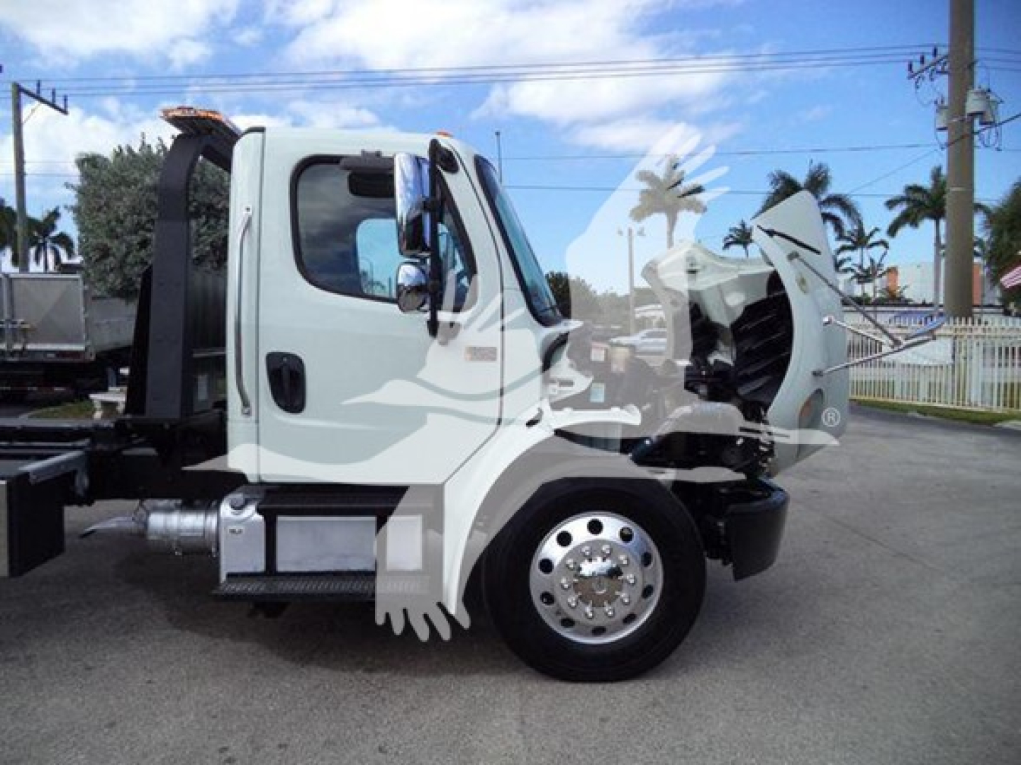 Freightliner Business Class M2 106 tow truck side view showing cab, front wheel, and rollback bed with open hood area.