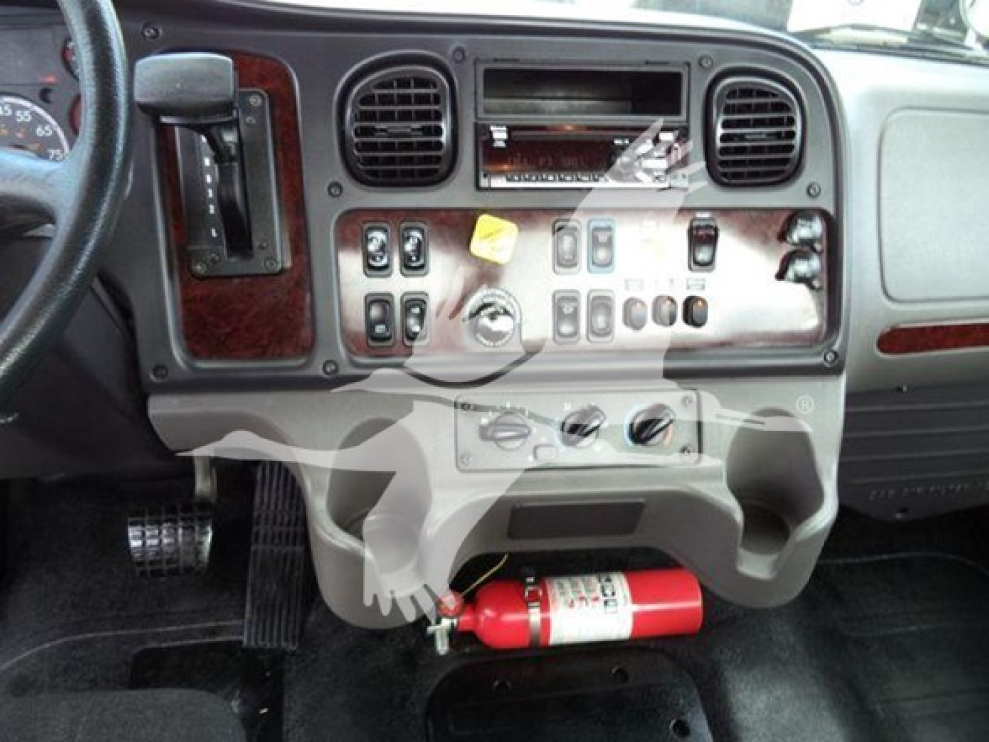 Dashboard of Freightliner M2 106 cab showing controls and a red fire extinguisher mounted under dash.