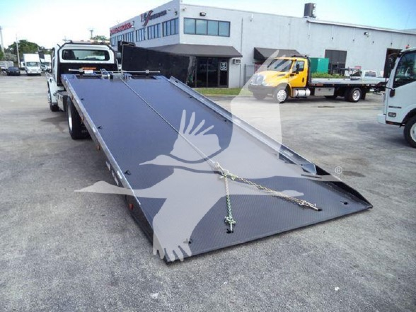 Flatbed tow truck ramp on a 2019 Freightliner Business Class M2 106 rollback showing loading bed and equipment in lot.