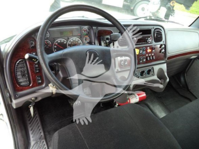 Dashboard and steering wheel of a Freightliner Business Class M2 106 interior with wood trim, gauges, control panel, and gear shifter visible.