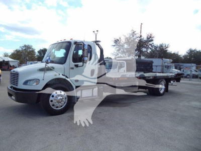Truck with flatbed rollback body, 2019 Freightliner Business Class M2 106, white cab, black bumper, long wheelbase, side view showing the vehicle at a lot.
